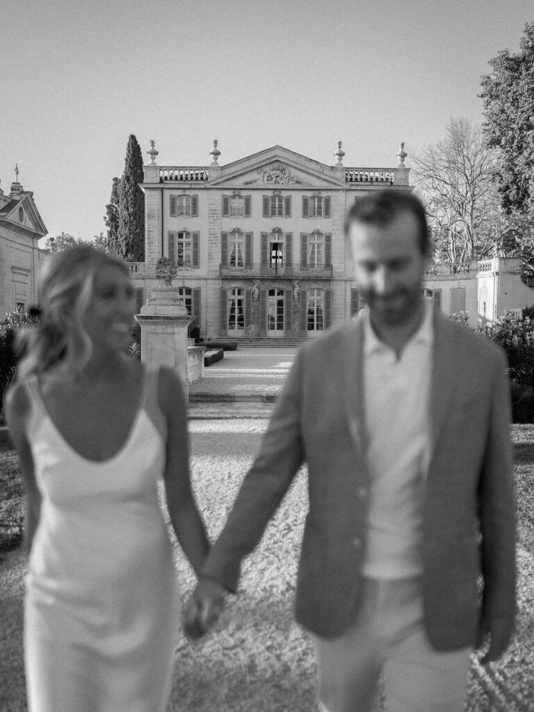 Bride and groom walking hand in hand in front of a historic Provence chateau, captured in an editorial destination wedding planned by a wedding planner in Provence.