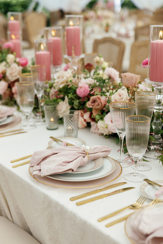 Reception table styled with blush linens, gold flatware, soft pink napkins, tapered candles, and garden-inspired floral centerpieces.