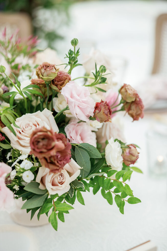 Close-up of a floral arrangement featuring blush roses, muted greenery, and organic textures styled for an elegant reception table.