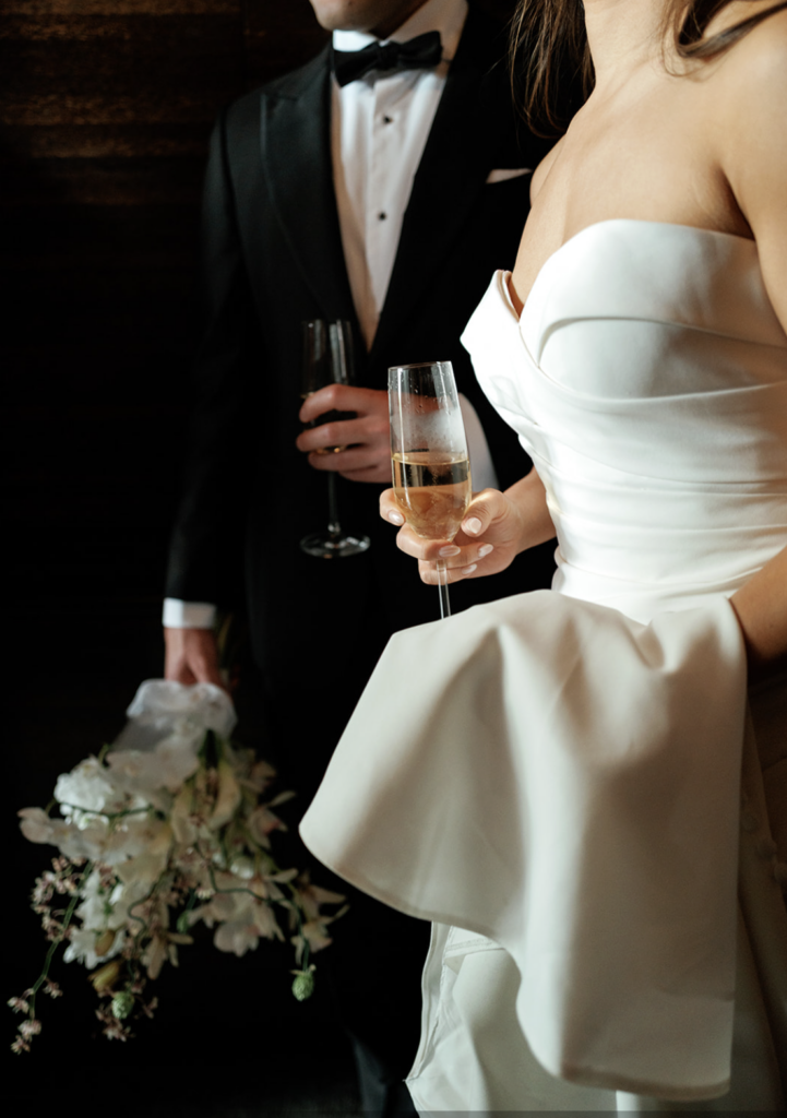 Bride and groom holding champagne glasses during a candlelit dinner, highlighting the seamless guest experience couples receive.