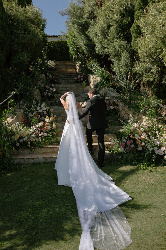 Bride and groom walking through a garden staircase surrounded by florals at a California destination wedding venue.