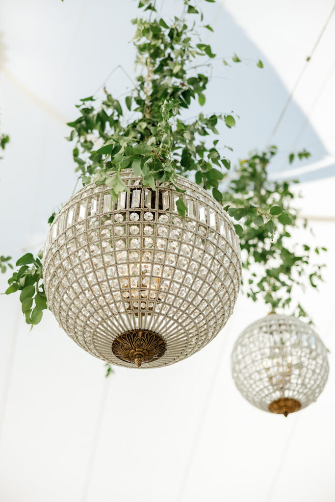 Crystal chandeliers suspended with greenery inside a coastal California wedding tent
