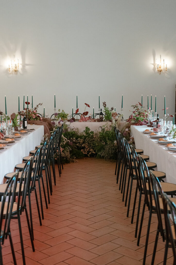 Long indoor dinner tables styled with florals and candles, creating an intimate wedding guest experience focused on shared moments.