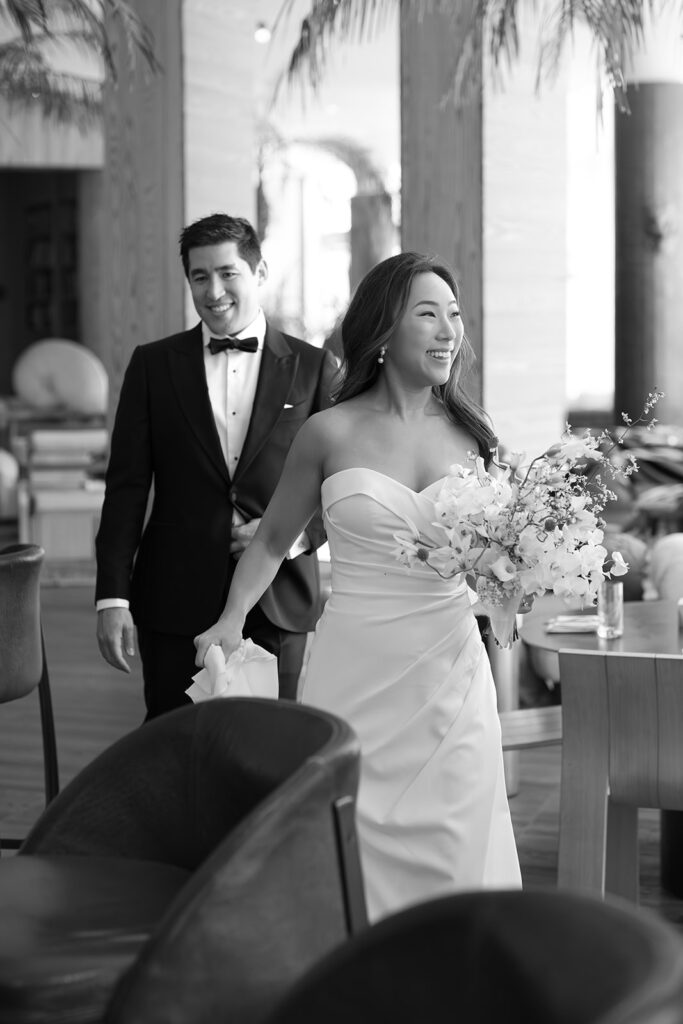 Bride and groom entering their wedding reception smiling with guests nearby, illustrating the ease and flow couples receive with full service wedding planning.