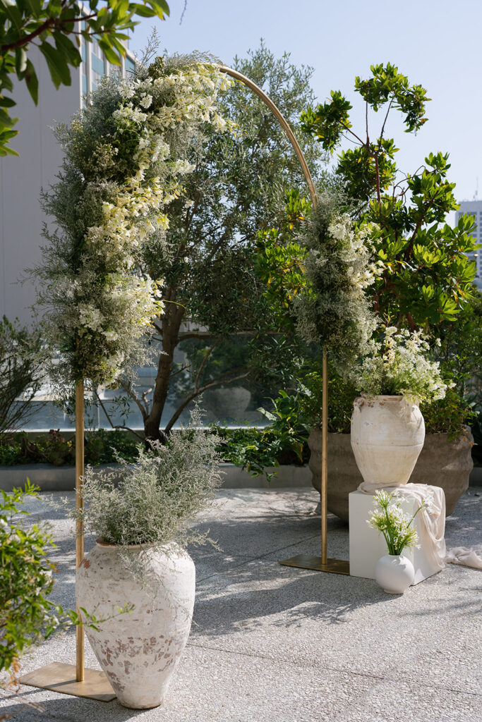 Floral ceremony arch with organic greenery and vessels designed for a luxury outdoor wedding setting.