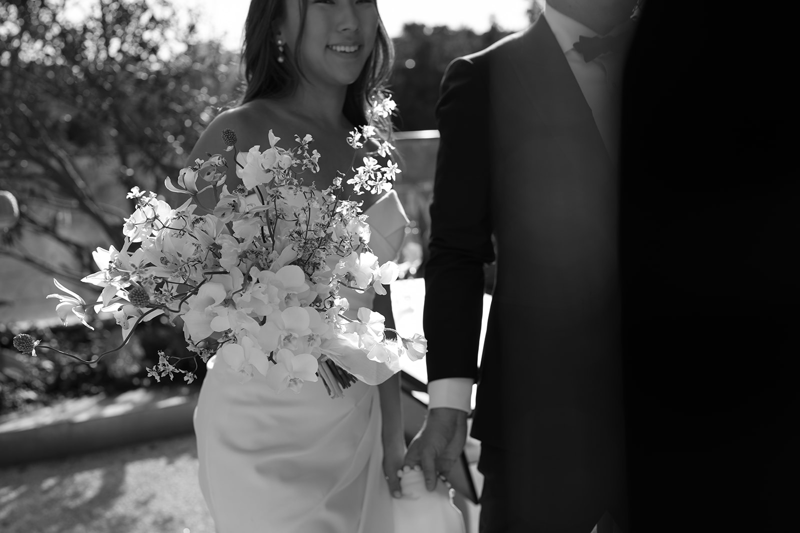 Bride and groom walking together outdoors holding a bouquet during a luxury outdoor wedding with refined floral design.