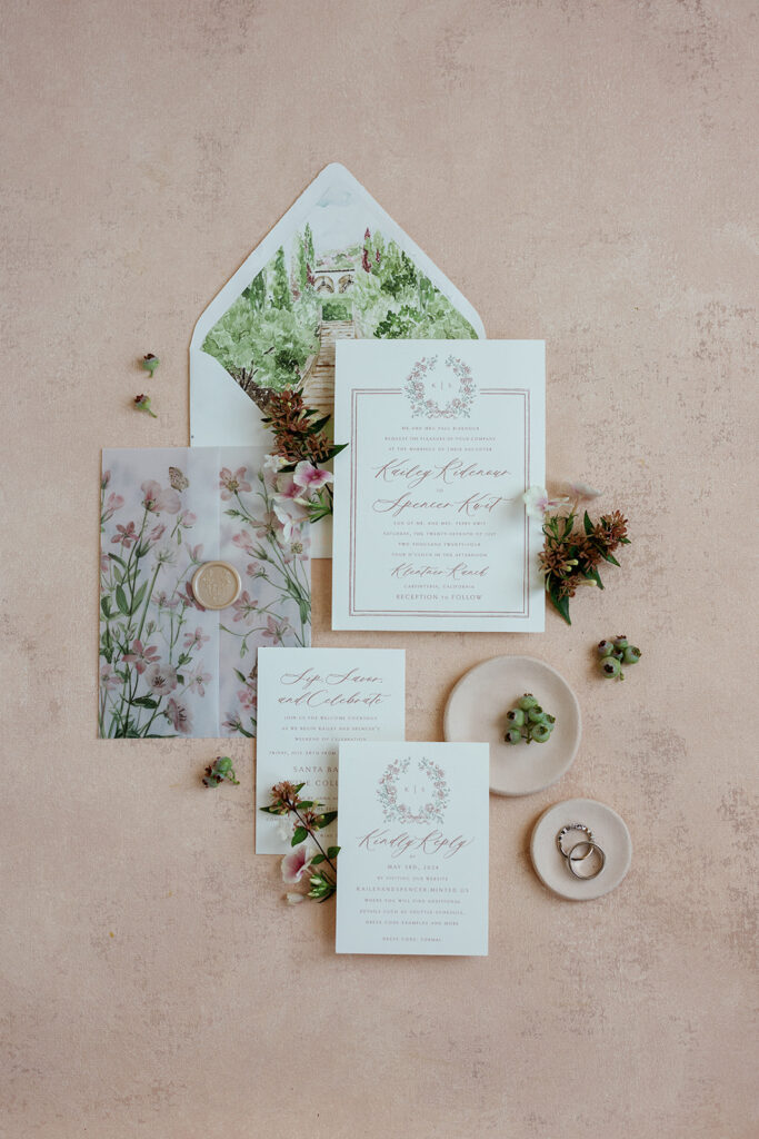 Flat lay of custom wedding stationery with floral illustrations, envelope liner, wax seal, and styling details photographed on a soft neutral backdrop.