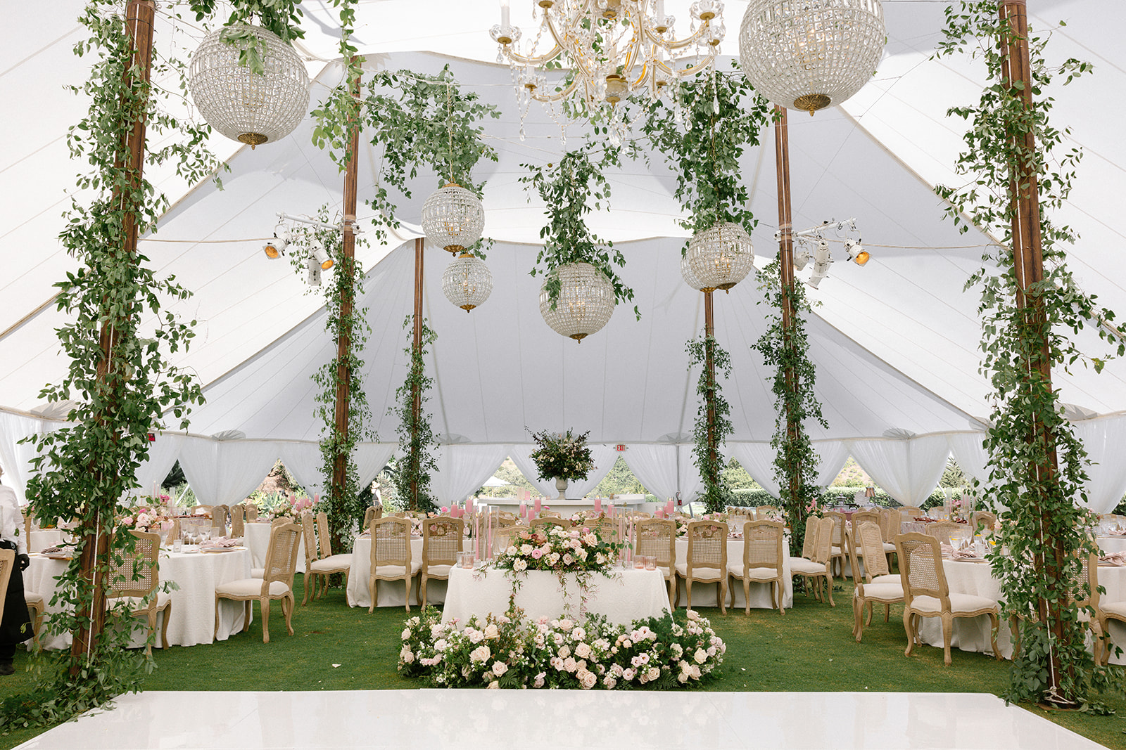 Elegant outdoor wedding reception under a sailcloth tent with chandeliers, greenery-wrapped poles, and refined table design planned by a Santa Barbara wedding planner.