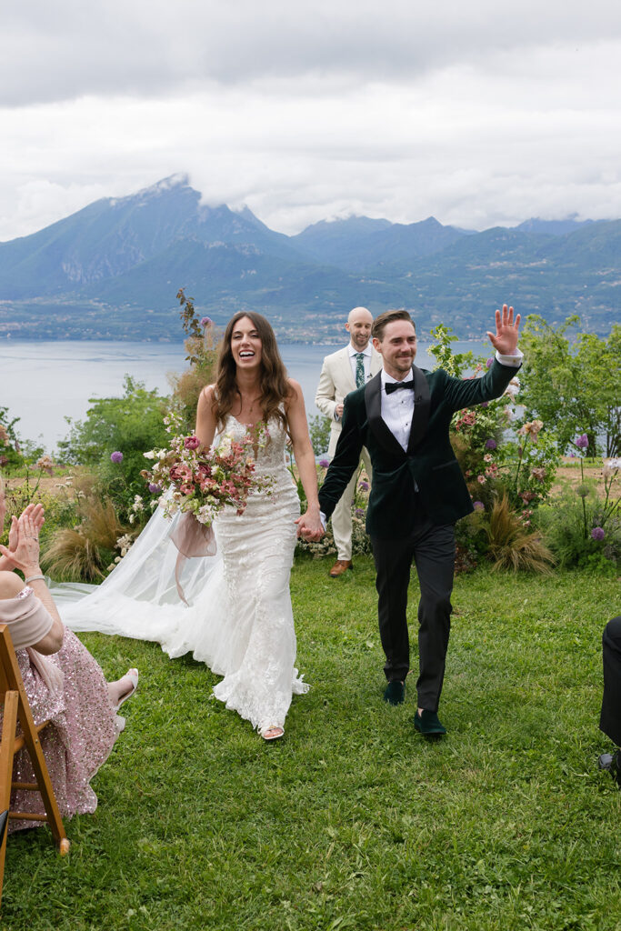 Bride and groom walking back down the aisle with guests cheering, marking a celebratory transition in the wedding day experience.