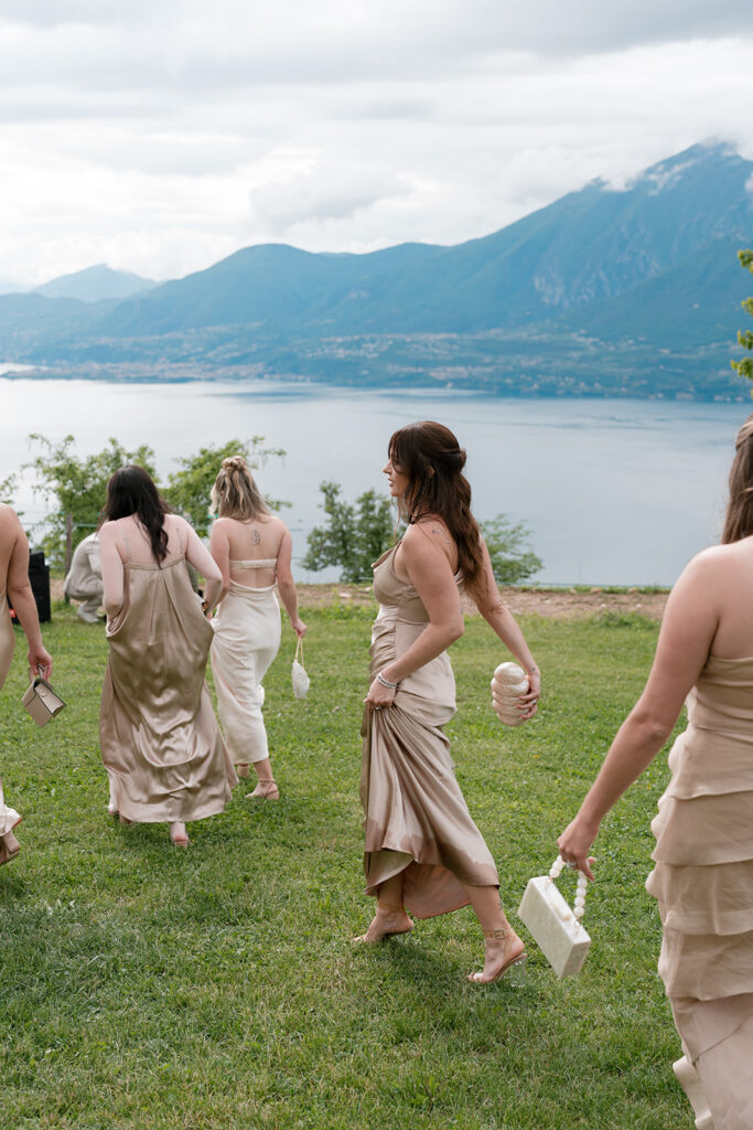 Bridesmaids in champagne satin gowns walk across a hillside overlooking a mountain lake, capturing the intimate atmosphere of a no phone wedding policy celebration.