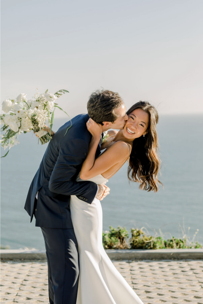 Bride and groom embracing at a California private estate wedding with ocean views in the background