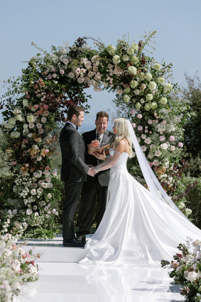 Bride and groom exchanging vows under a lush floral arch at a Santa Barbara wine country wedding venue