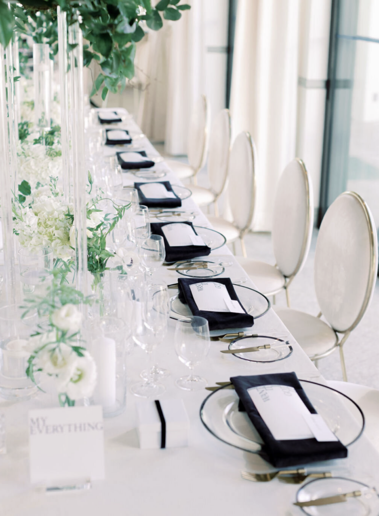Modern California wedding reception with long table, clear ghost chairs, black napkins, and tall floral centerpieces