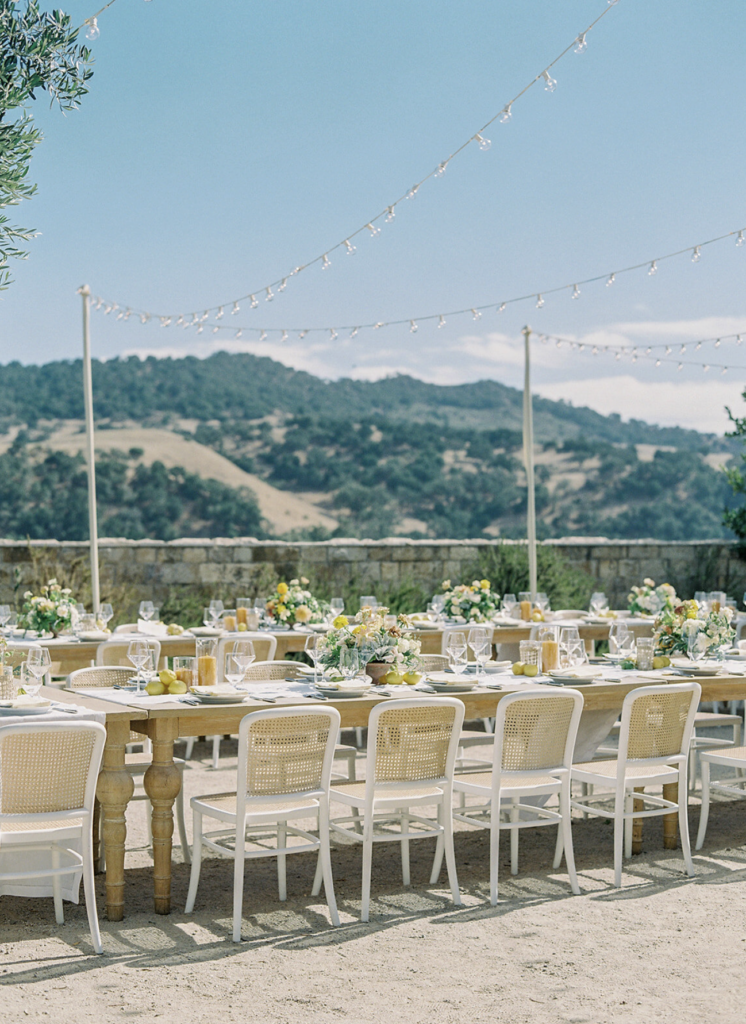 Outdoor wedding reception with long farm tables set against rolling California hills, string lights overhead, planned by an experienced wedding planner