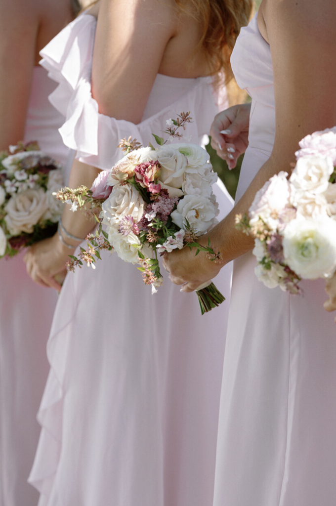 Bridesmaids in blush ruffled dresses holding white and pink floral bouquets at a California wedding