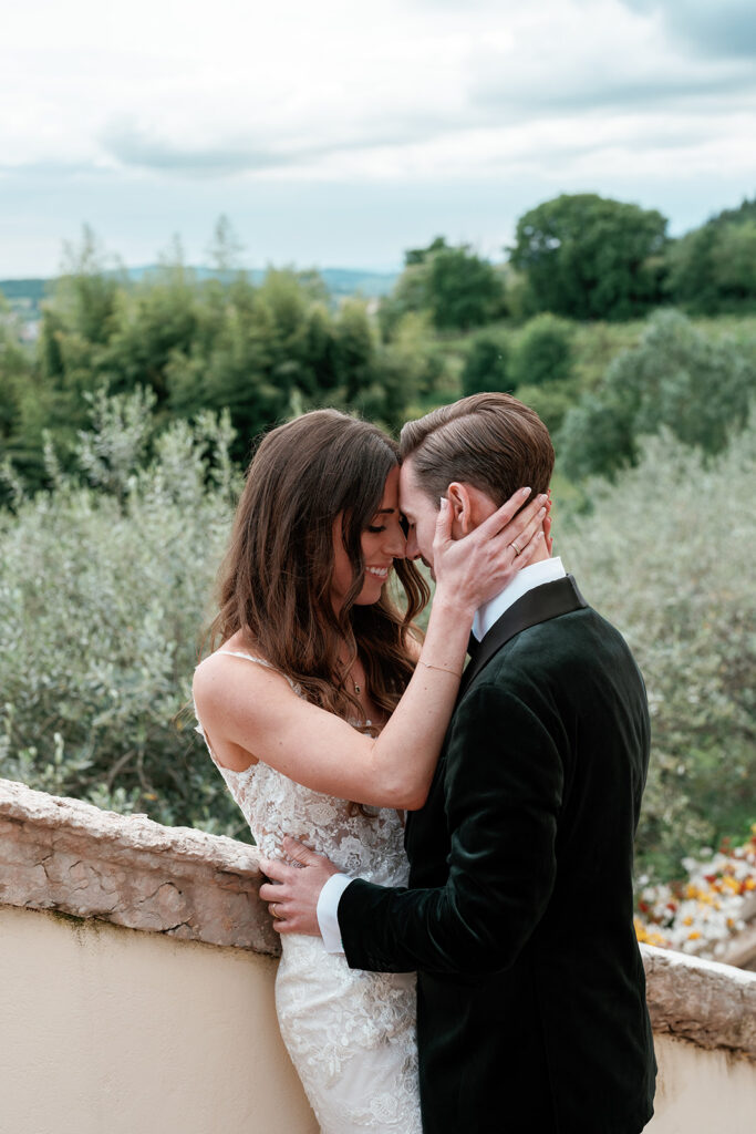 Bride and groom resting their foreheads together on a stone terrace surrounded by olive trees at an Italian destination wedding