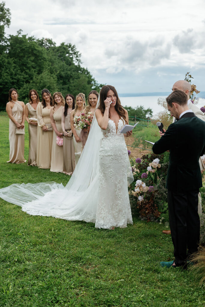 Bride wiping a tear during an outdoor hillside ceremony with bridesmaids in champagne dresses looking on, the kind of seamless moment that follows when you interview a wedding planner well
