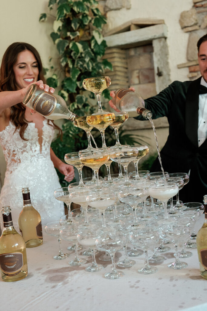 Bride and groom pouring Italian sparkling wine over a coupe glass champagne tower together at their wedding reception