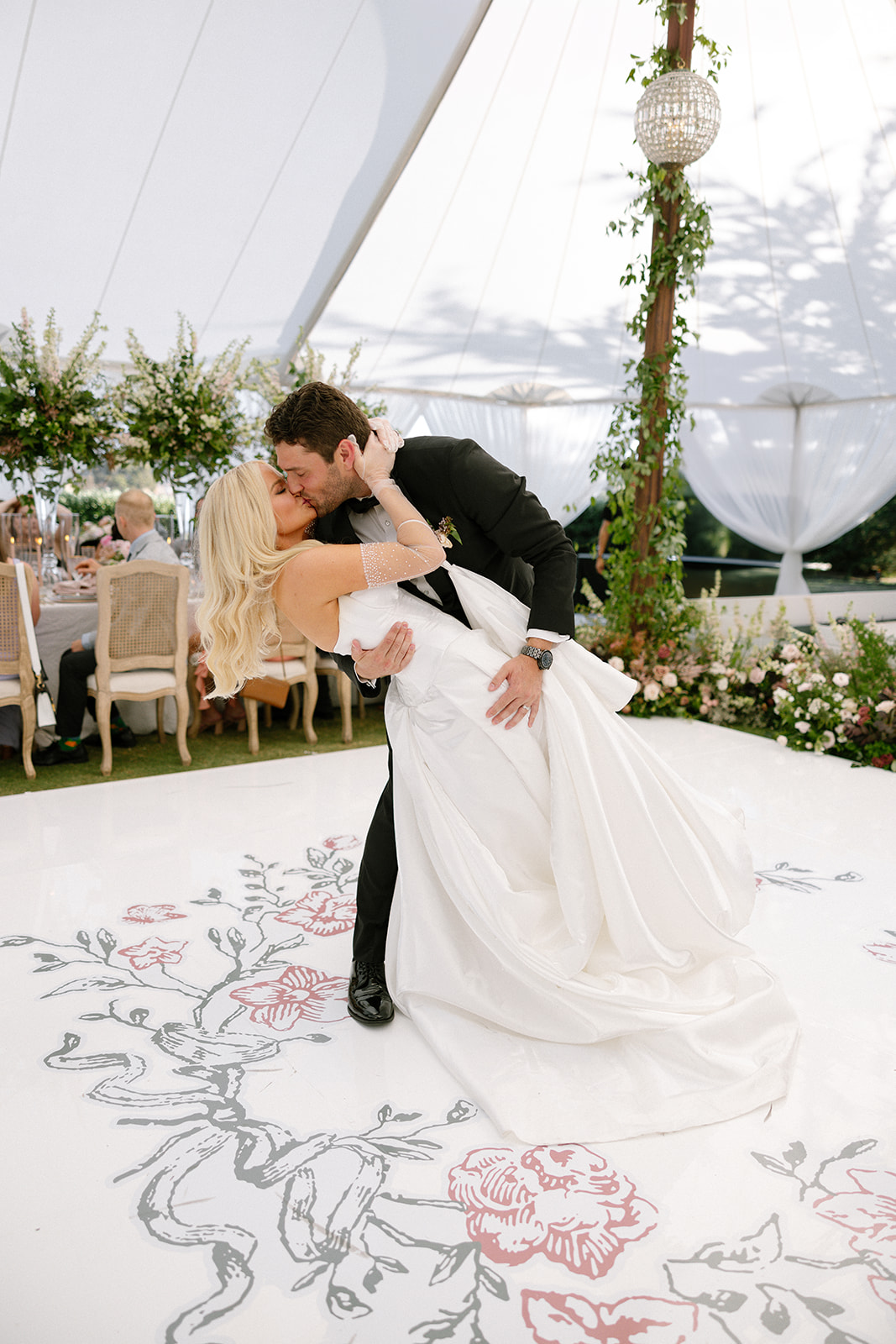 Bride and groom kissing in a dip on a hand-painted floral dance floor under a sailcloth tent with a crystal chandelier