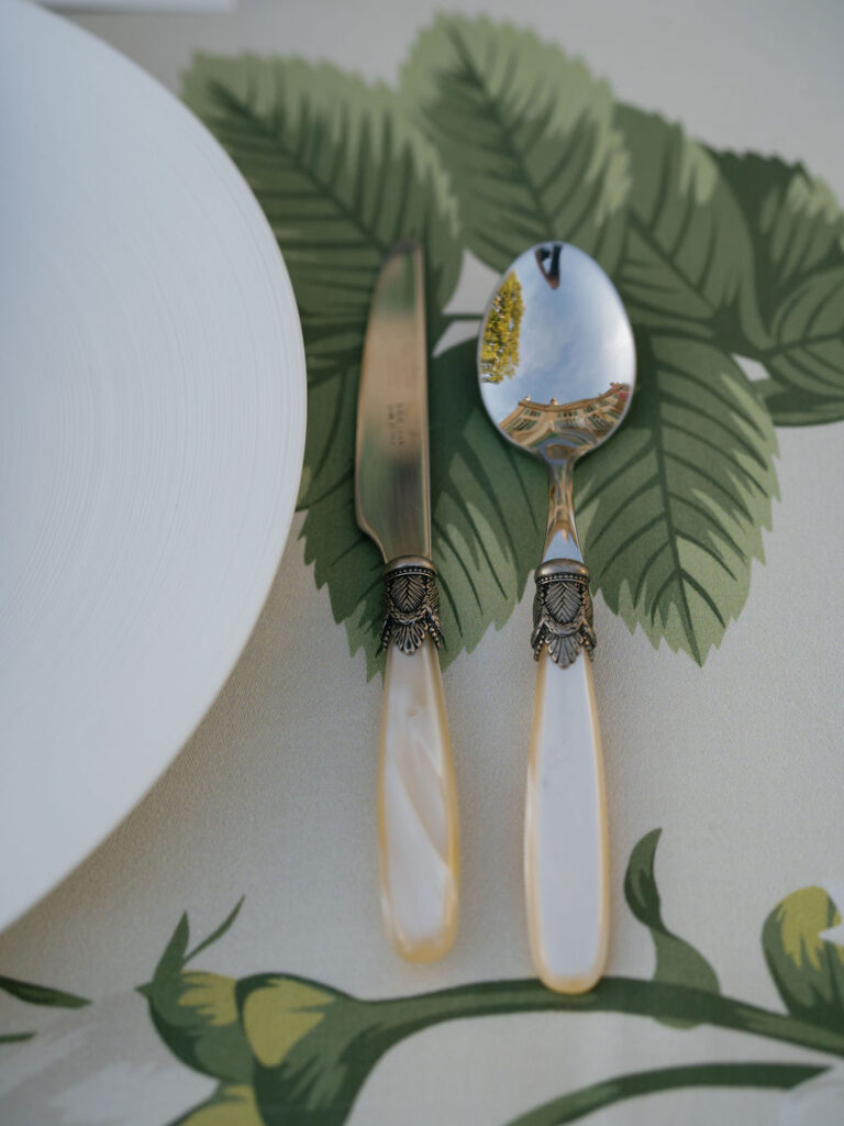 Wedding place setting with a block-print floral napkin, wood-handled forks, and a place card, styled with heirloom squash and trailing amaranthus for an elevated table